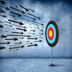 Oncoming arrows, large and small, are about to bombard bullseye on target. The target is attached to a stand.