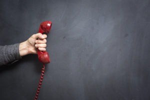 Human hand holding telephone on blackboard - Contact Us.